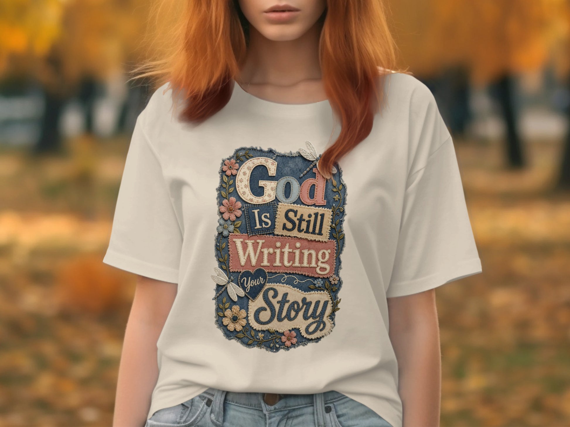 White t-shirt with "God Is Still Writing Your Story" text and floral embellishments.