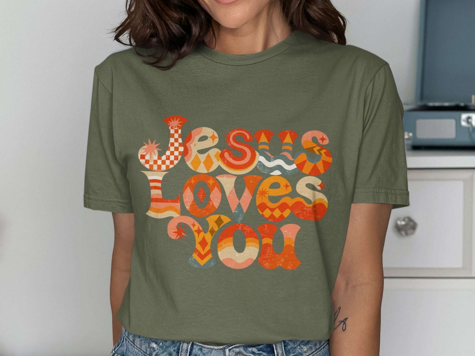 Olive green t-shirt with "Jesus Loves You" in colorful retro lettering.