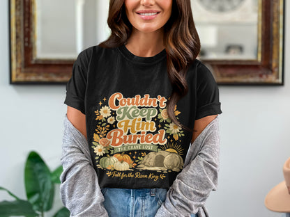 Black t-shirt with "Couldn't Keep Him Buried" text, tomb, pumpkins, and flowers.