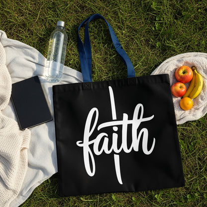 Black tote bag with white "faith" script, picnic items on grass.