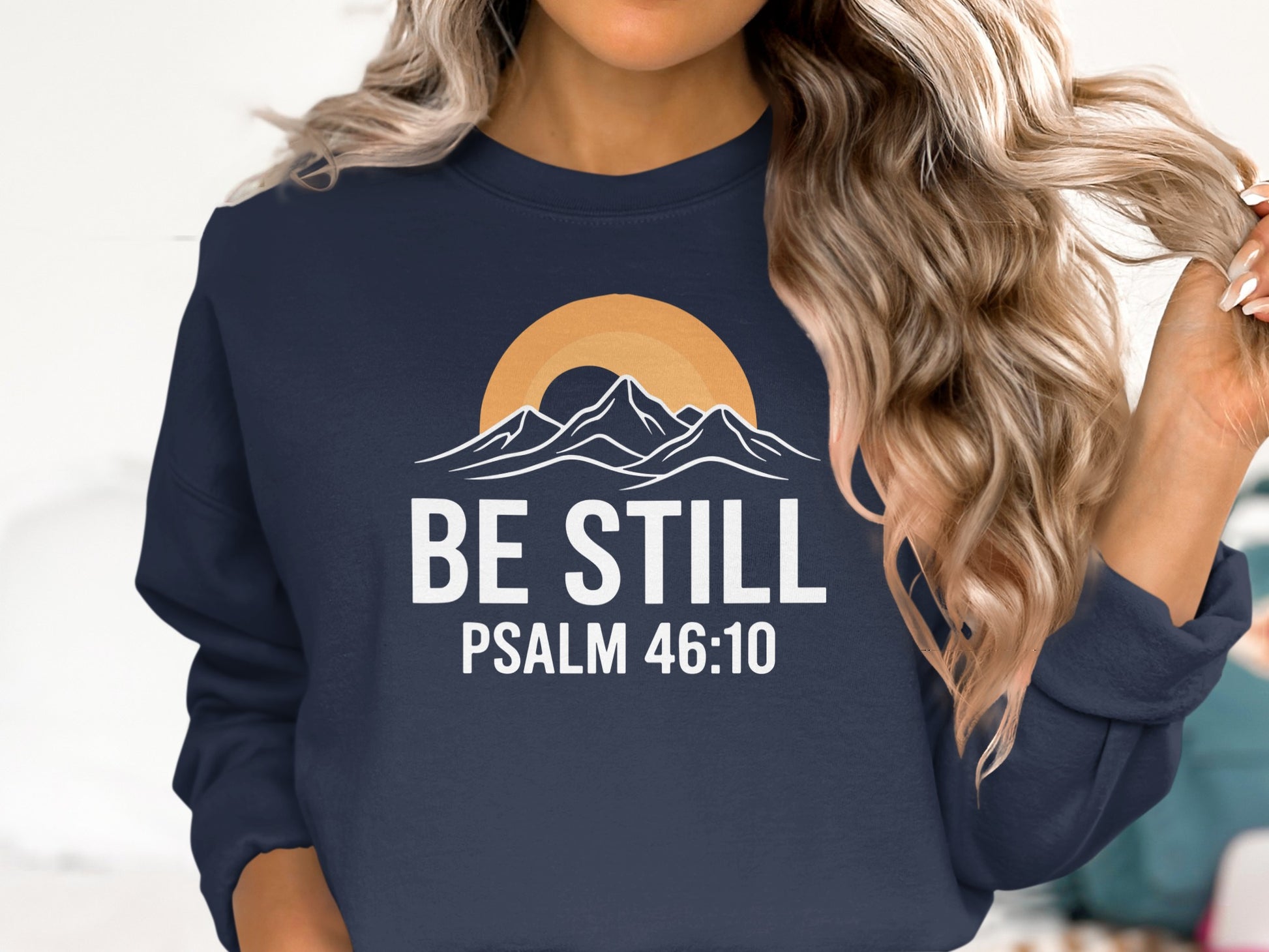 Navy sweatshirt with "Be Still" and "Psalm 46:10" text and mountain sunset graphic.