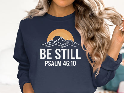 Navy sweatshirt with "Be Still" and "Psalm 46:10" text and mountain sunset graphic.