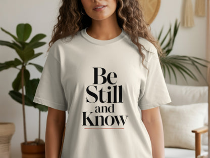 Cream t-shirt with black text reading "Be Still and Know" with an orange line.