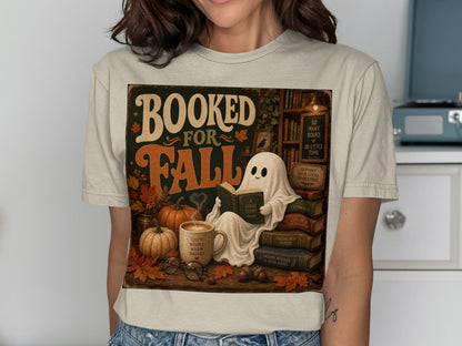 Booked for Fall t-shirt with a ghost reading next to pumpkins and books.