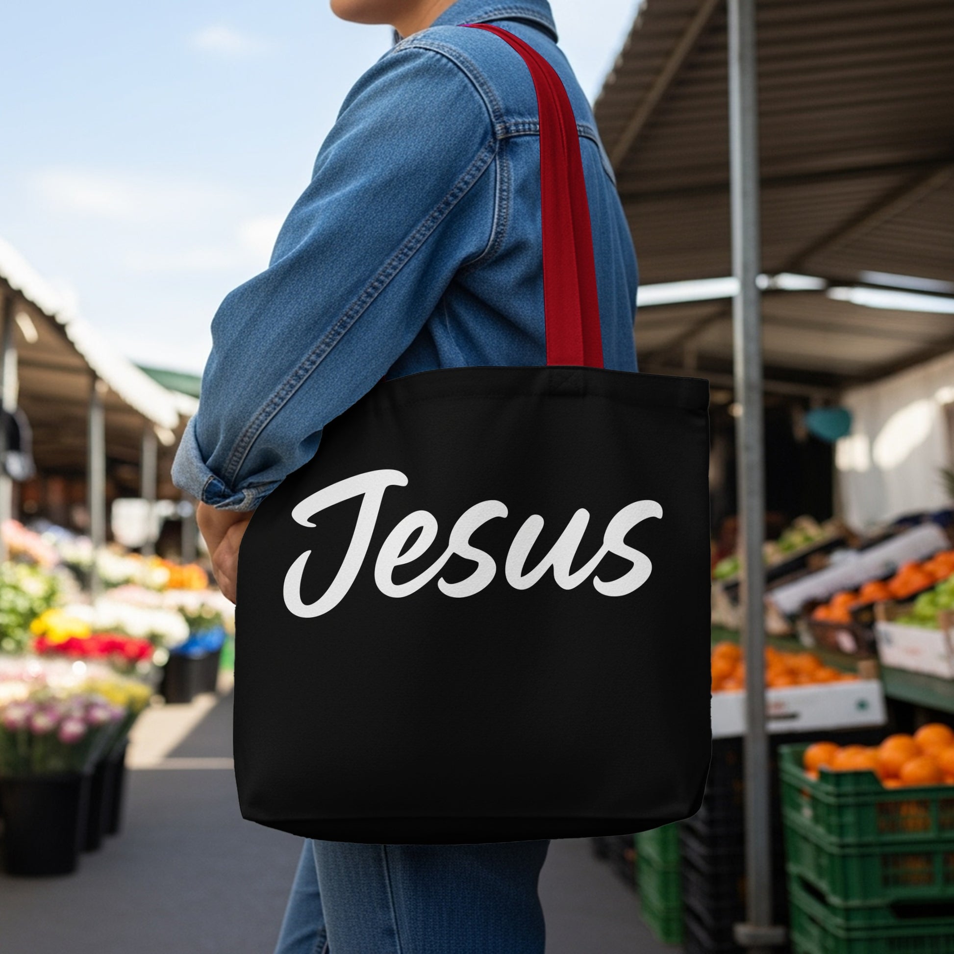 Black tote bag with "Jesus" in white cursive font, held by a person.