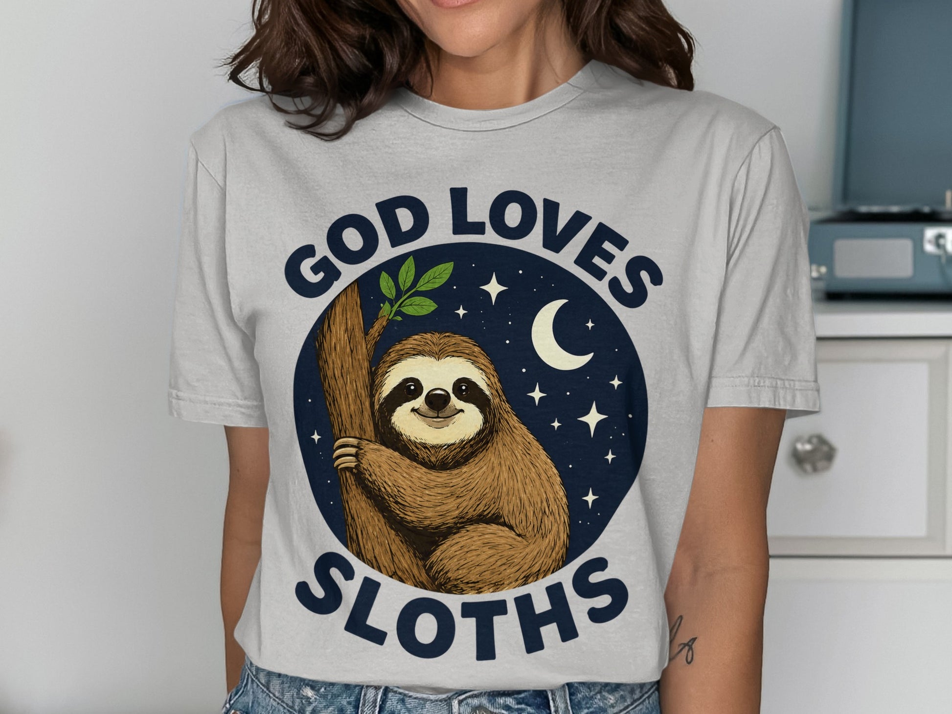 Sloth hanging on tree branch, moon and stars, "God Loves Sloths" text.