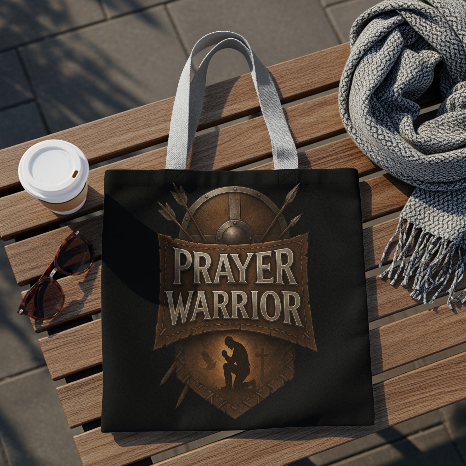 Black tote bag with "Prayer Warrior" text and kneeling silhouette on a wooden bench.