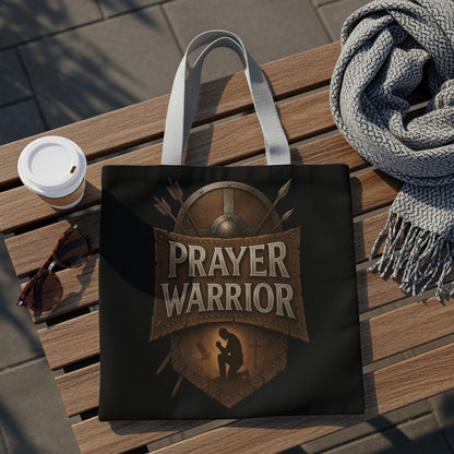 Black tote bag with "Prayer Warrior" text and kneeling silhouette on a wooden bench.
