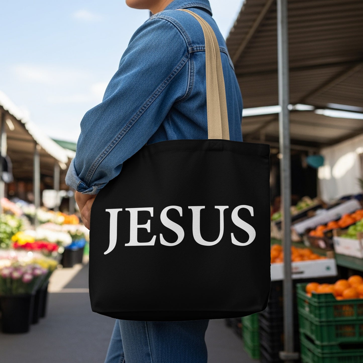 Black tote bag with "JESUS" in large white text, worn by a person outdoors.