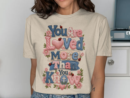 T-shirt with "You Are Loved More Than You Know" text and heart and floral accents.