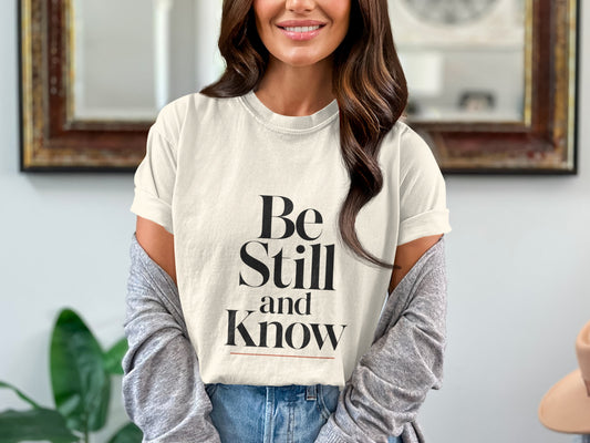 Cream t-shirt with "Be Still and Know" text and a red underline.