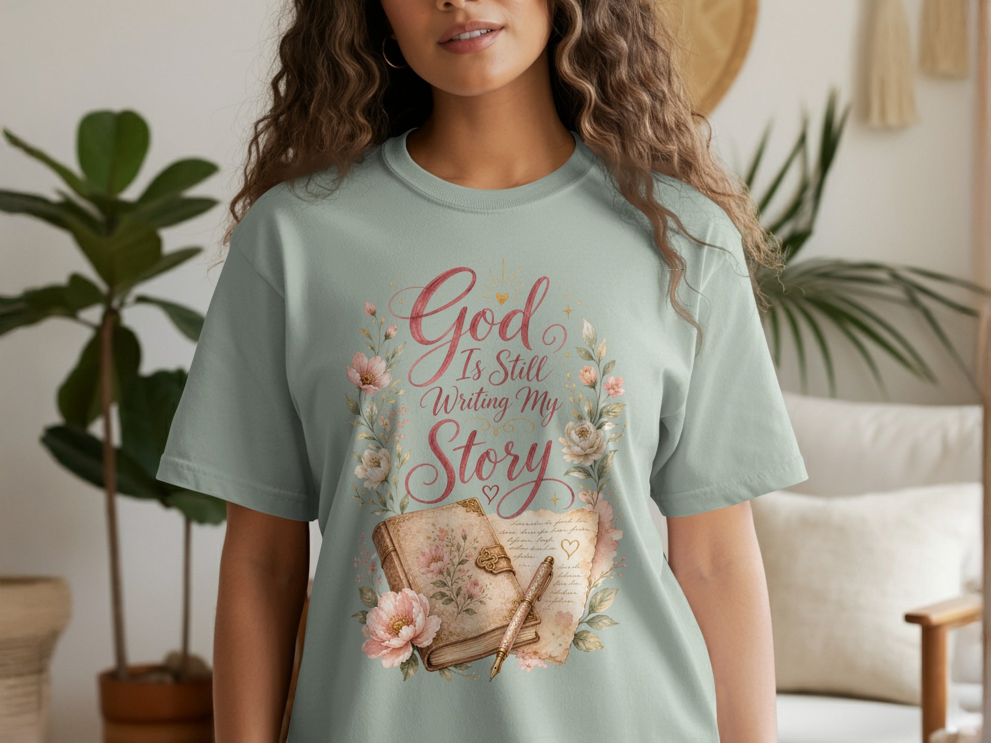 "God Is Still Writing My Story" text with floral and book design on a light green t-shirt.