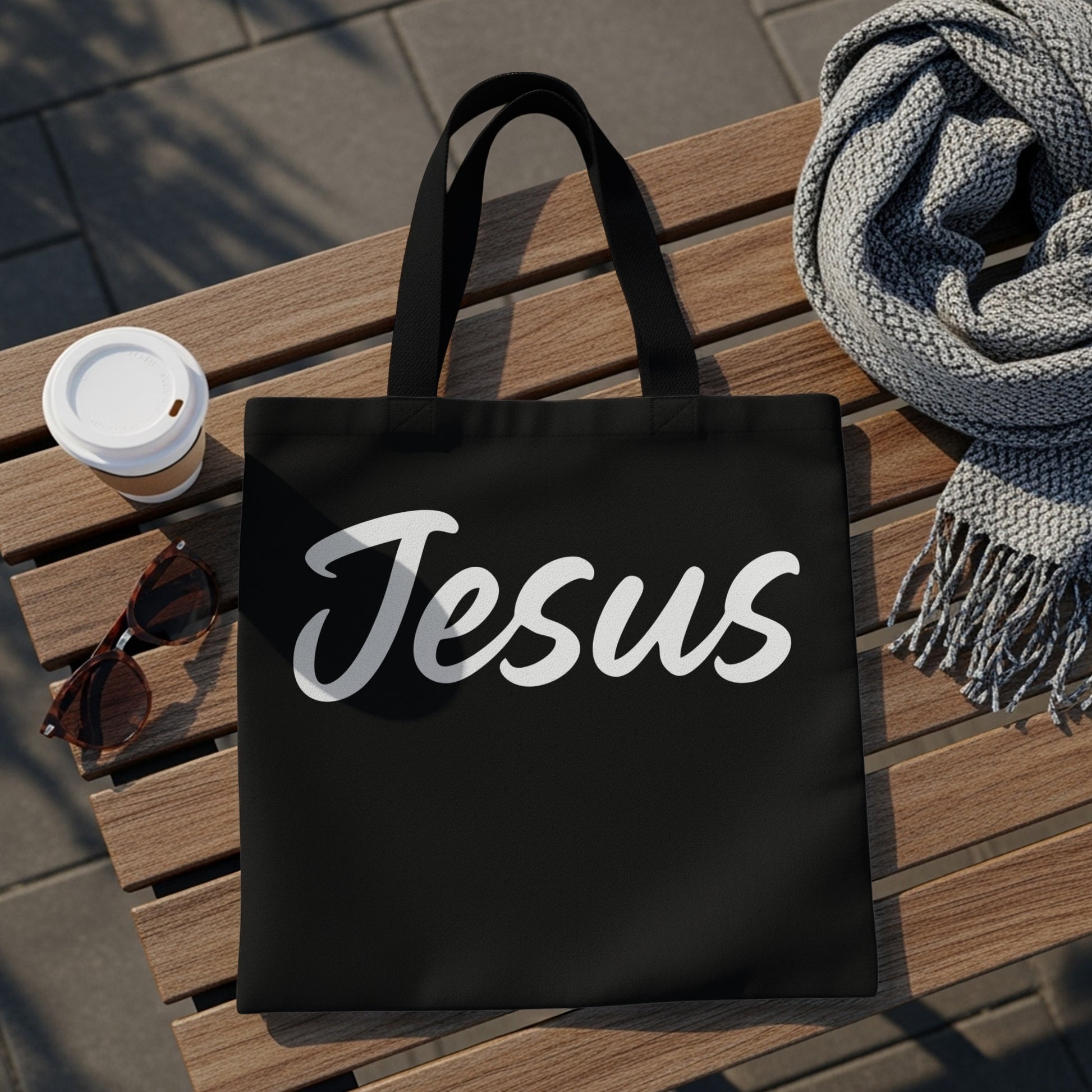 Black tote bag with white "Jesus" text, sunglasses, and coffee cup.