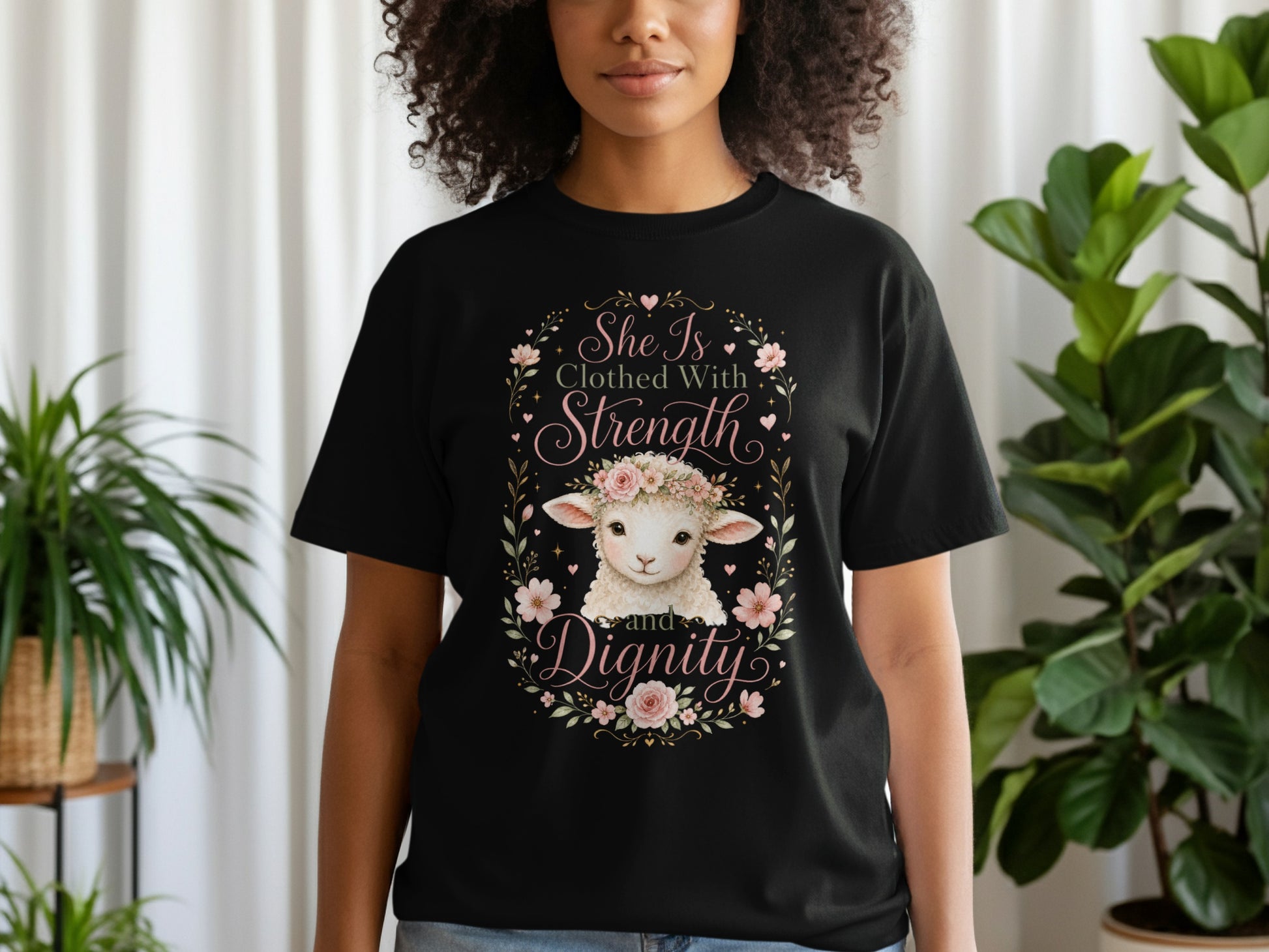 Black t-shirt with a floral wreath framing a sheep and the text "She Is Clothed With Strength and Dignity."