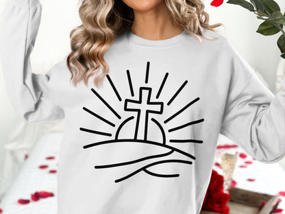 White sweatshirt with a black line drawing of a cross rising over a hill with sun rays.