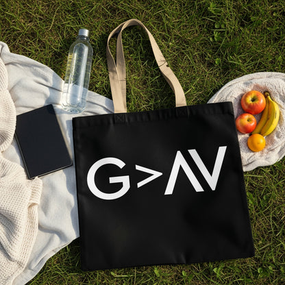 Black tote bag with white "G > AV" graphic, on grass with fruit and water bottle.