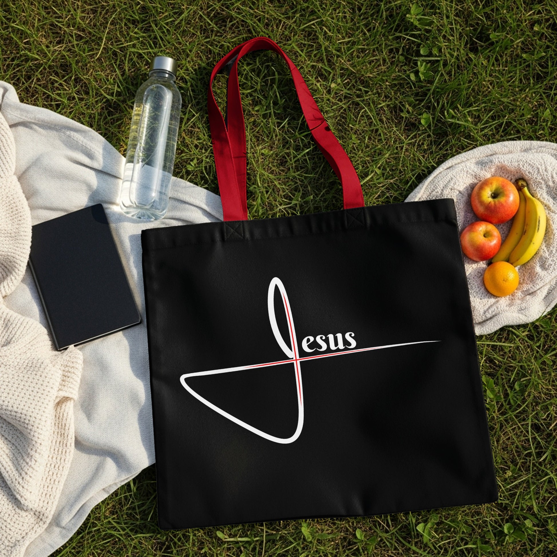 Black tote bag with red straps, featuring white text "Jesus" and a red cross.