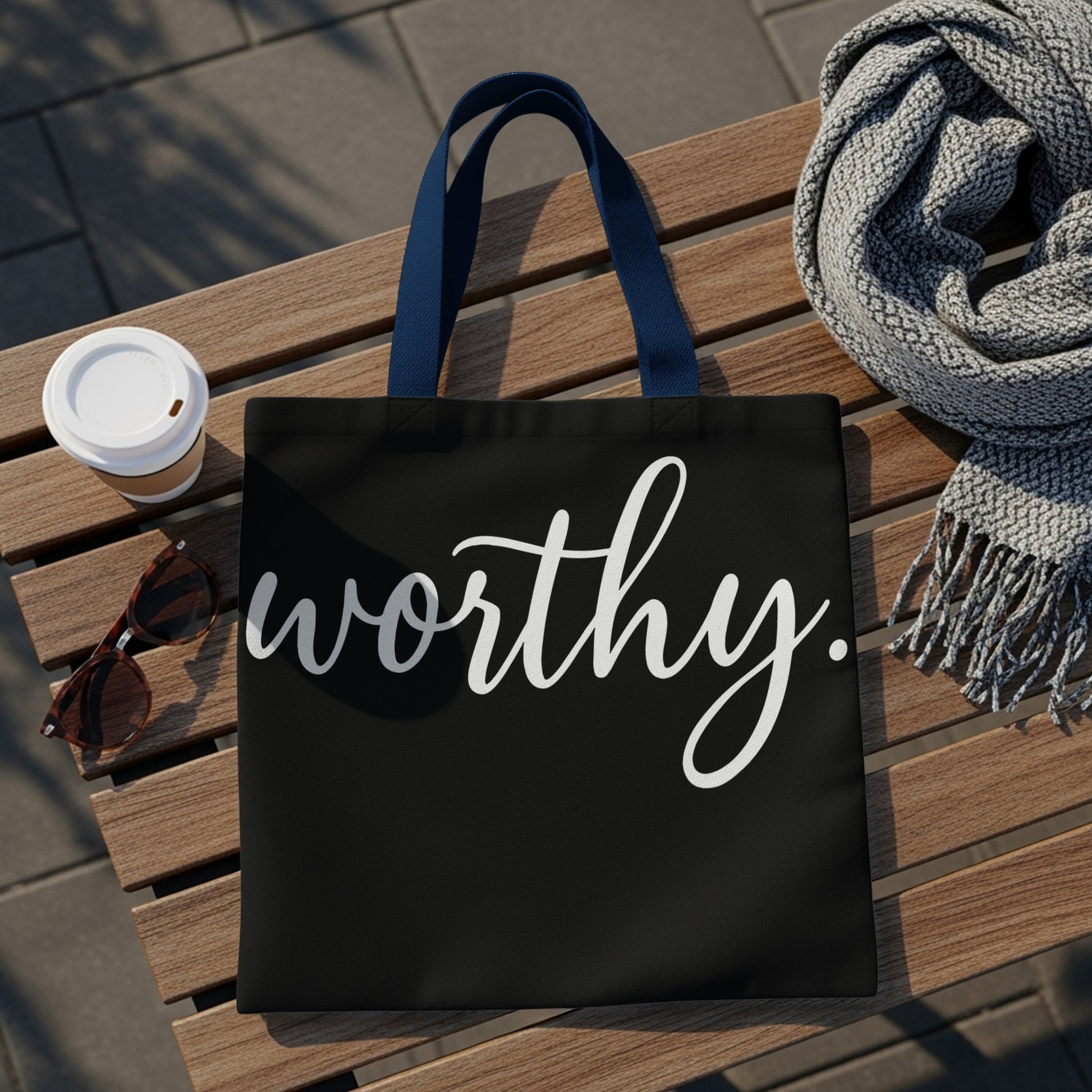 Black tote bag with "worthy." in white cursive text, navy handles.