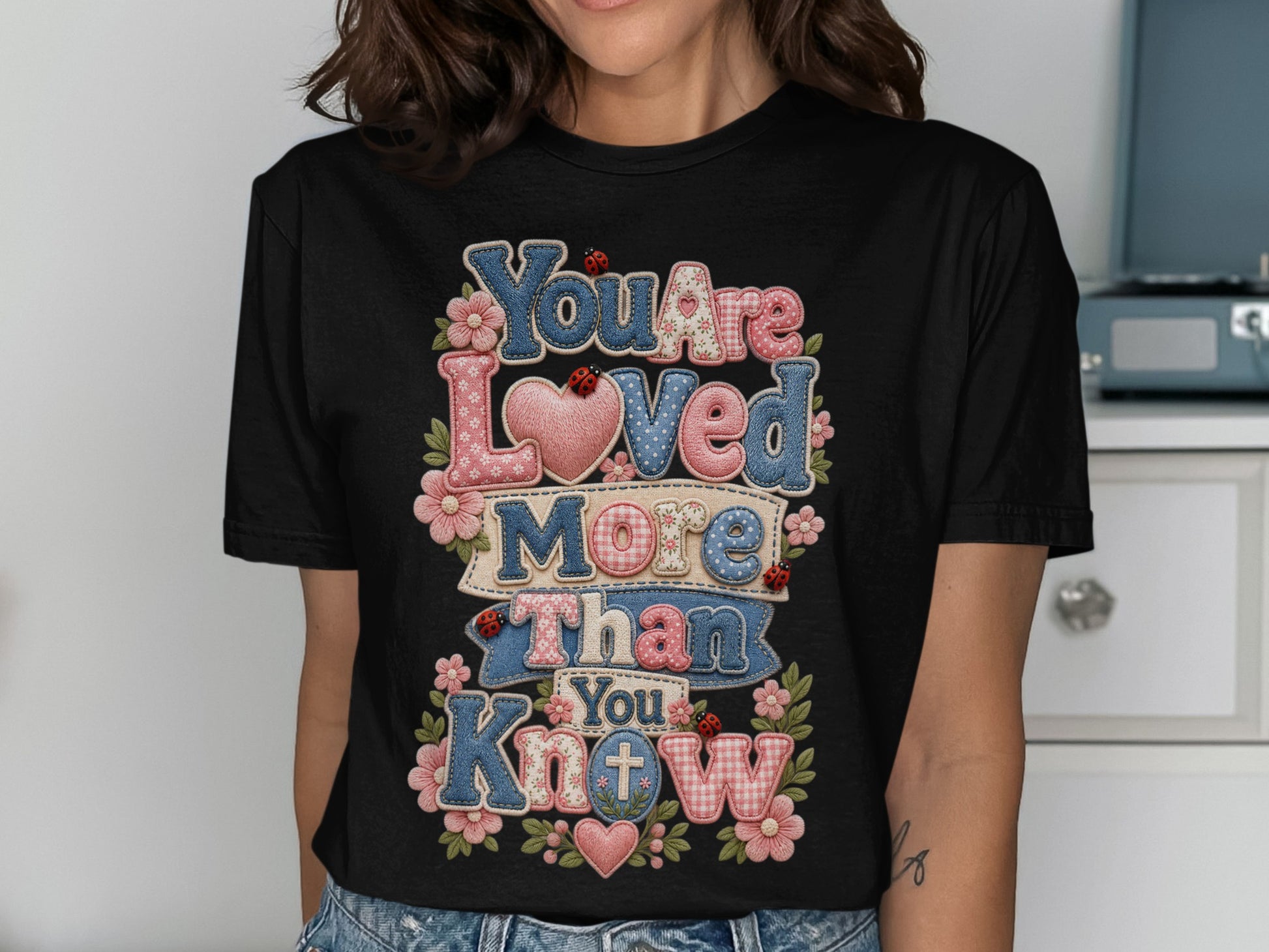 Black t-shirt with "You Are Loved More Than You Know" text in colorful patchwork and heart designs.
