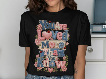 Black t-shirt with "You Are Loved More Than You Know" text in colorful patchwork and heart designs.