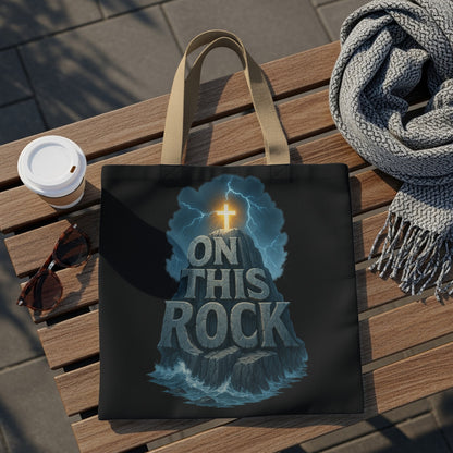 Black tote bag with a graphic of a glowing cross atop a rocky outcrop reading "ON THIS ROCK".