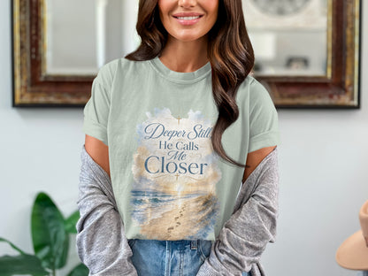 Light green t-shirt with beach and cloud graphic saying "Deeper Still, He Calls Me Closer."