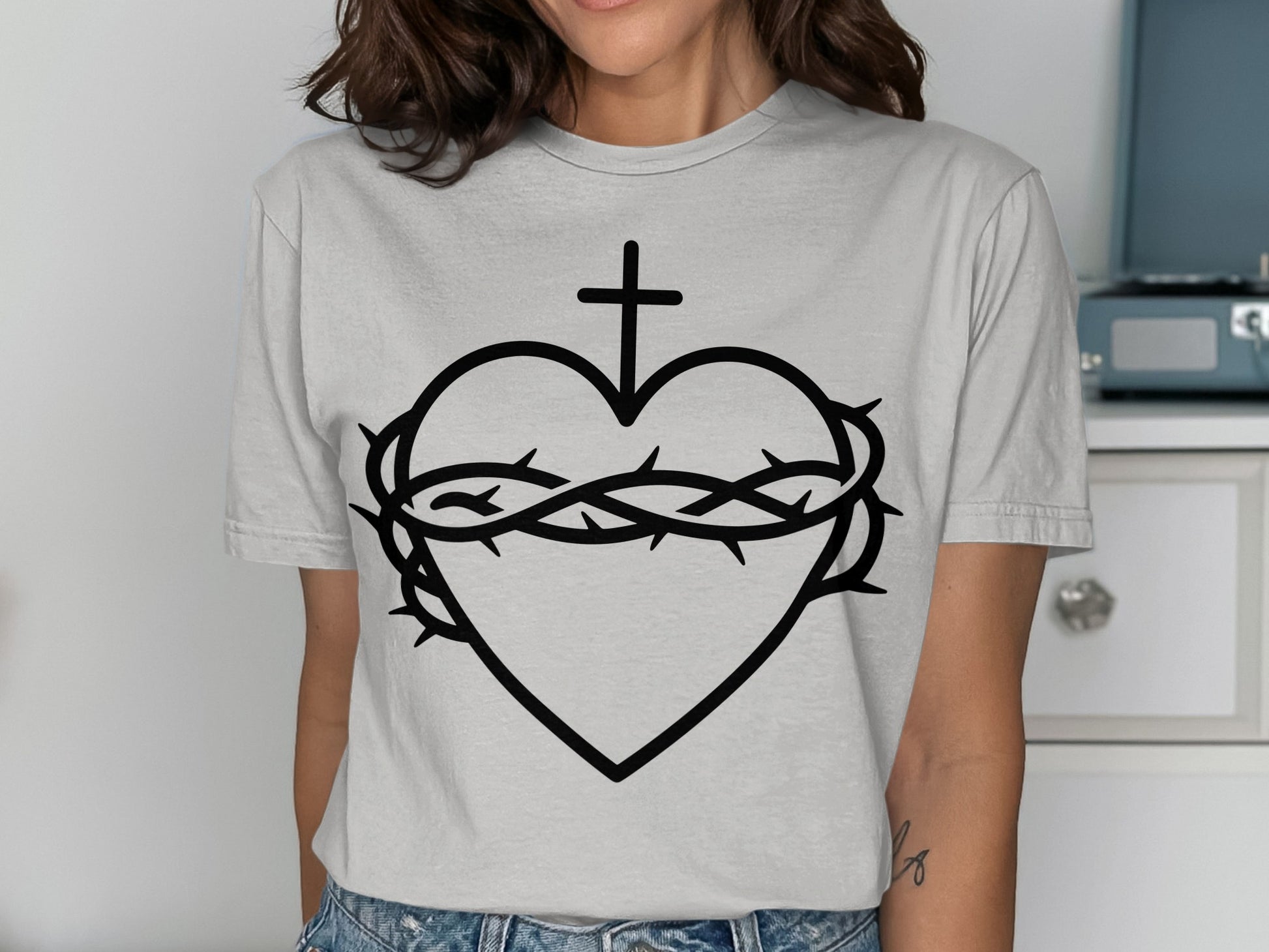 Black heart with crown of thorns and cross, on a light grey t-shirt.