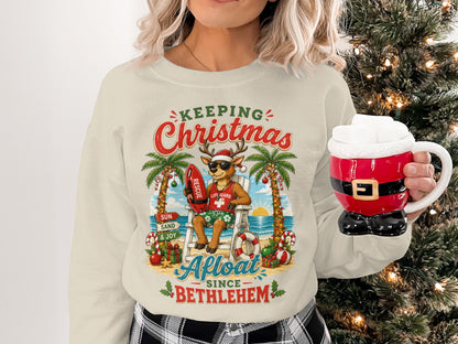 Cream sweatshirt with a holiday graphic of a reindeer lifeguard at a beach.