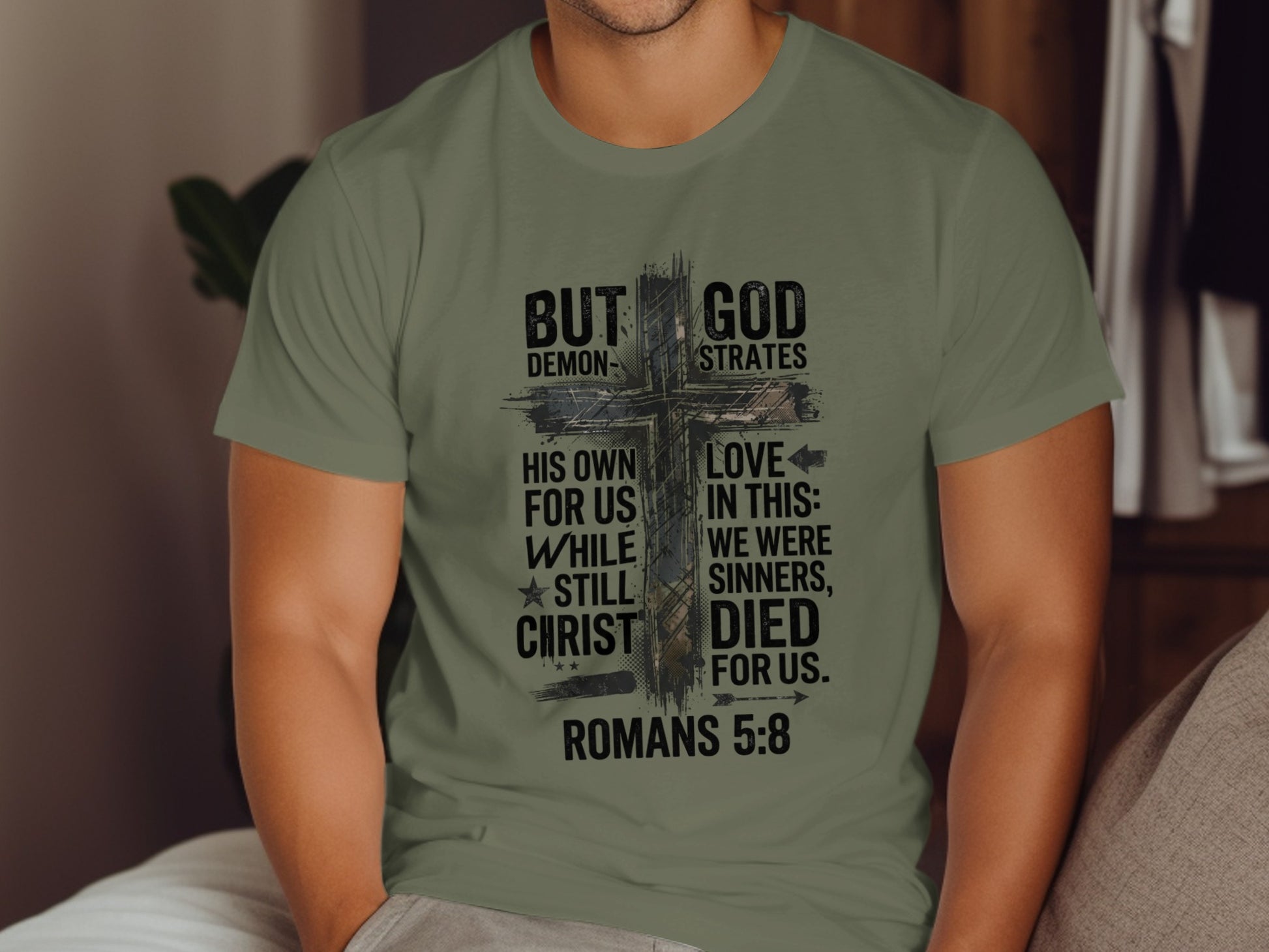 Olive green t-shirt with "But God Demonstrates His Love For Us While Christ Still Died For Us. Romans 5:8" graphic.