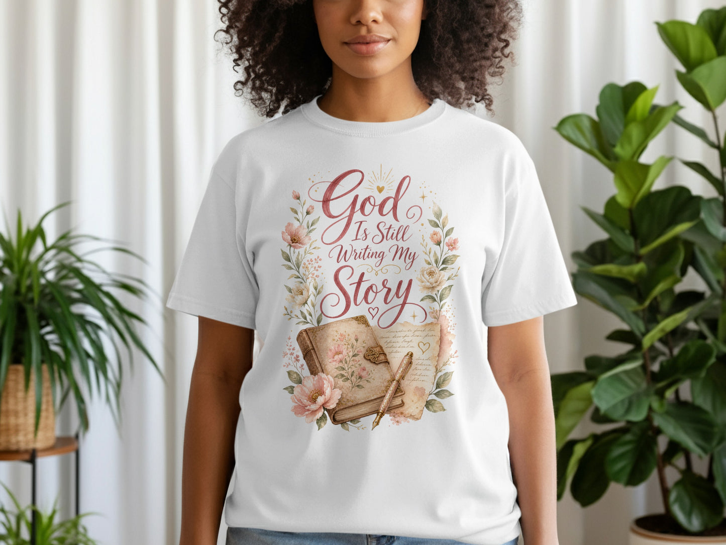 White t-shirt with "God Is Still Writing My Story" in script, surrounded by floral design.
