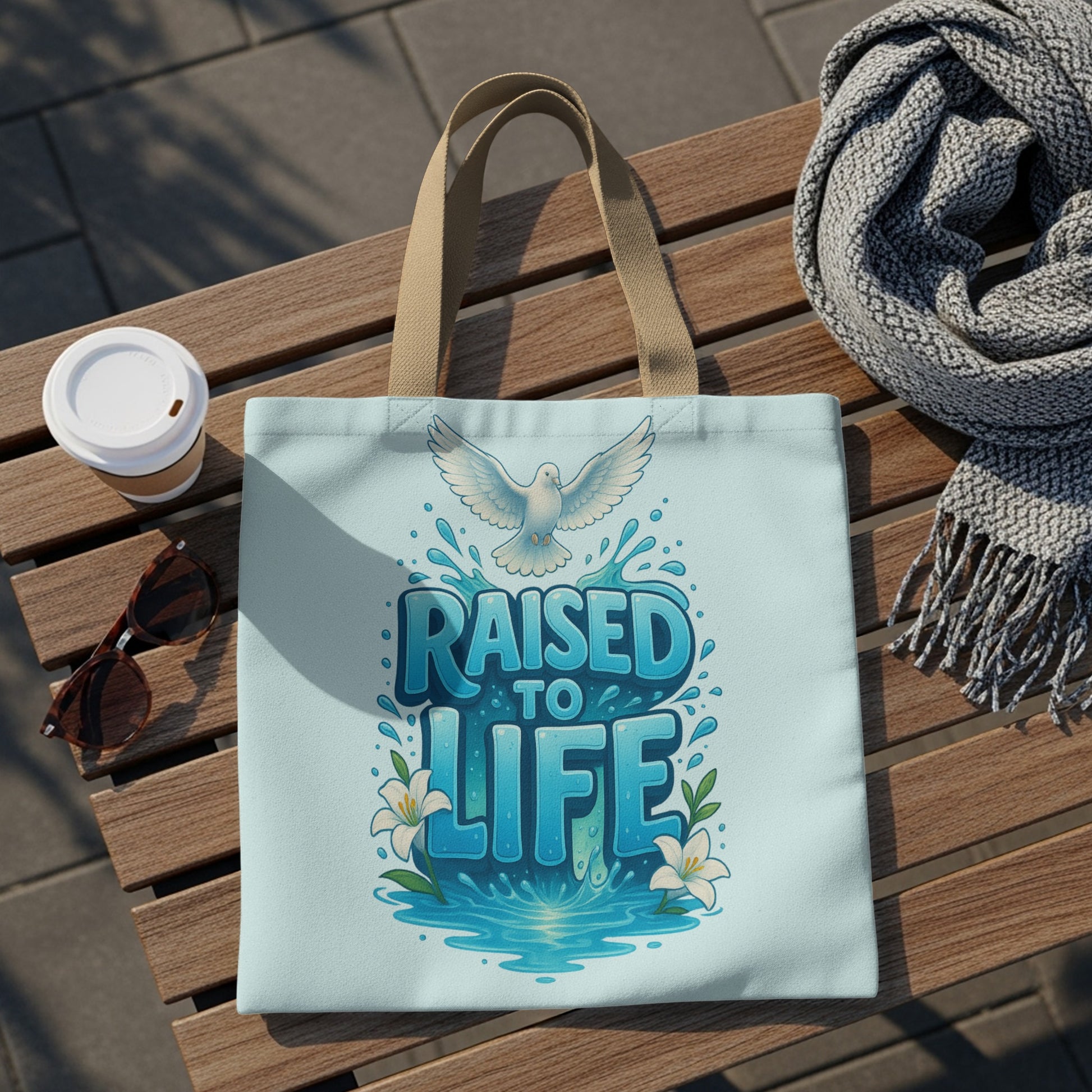 Light blue tote bag with a dove, water splash, and "RAISED TO LIFE" text.