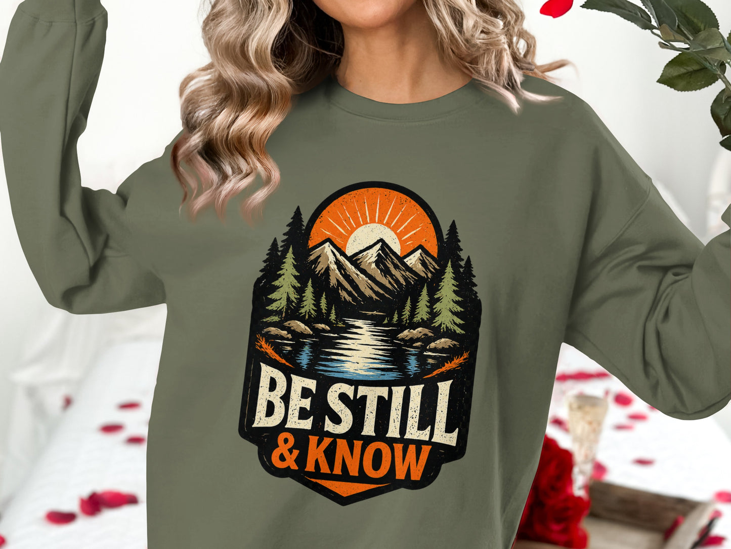 Olive green sweatshirt with mountains, lake, trees, and "Be Still & Know" text.