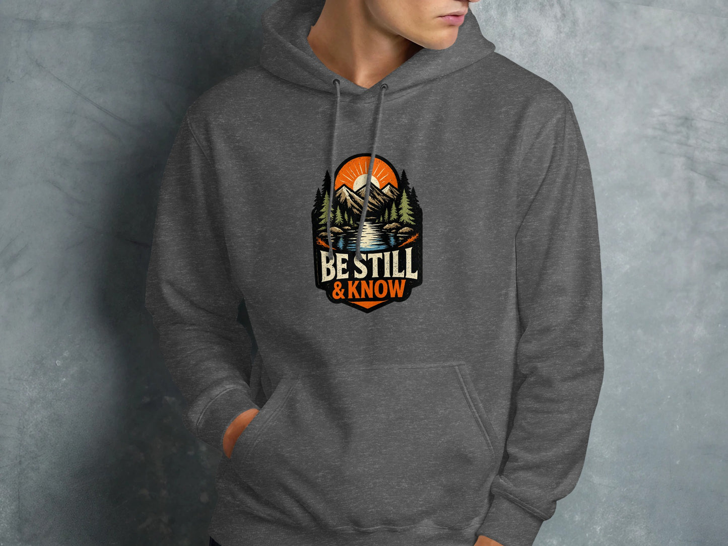 Dark gray hoodie with mountainous landscape and "Be Still & Know" text.