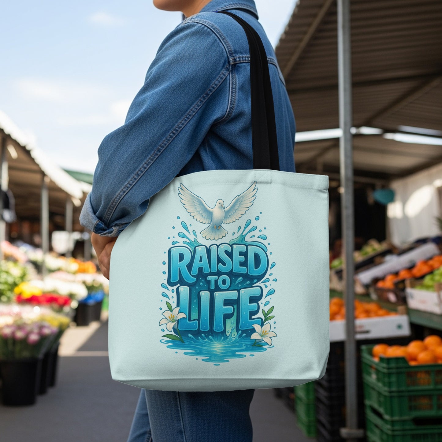 Tote bag with white dove and text "RAISED TO LIFE" on a light blue background.