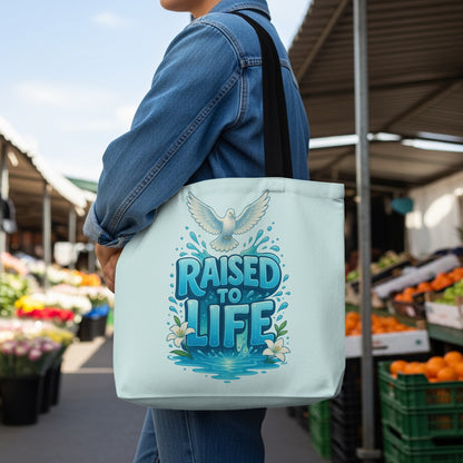 Tote bag with white dove and text "RAISED TO LIFE" on a light blue background.