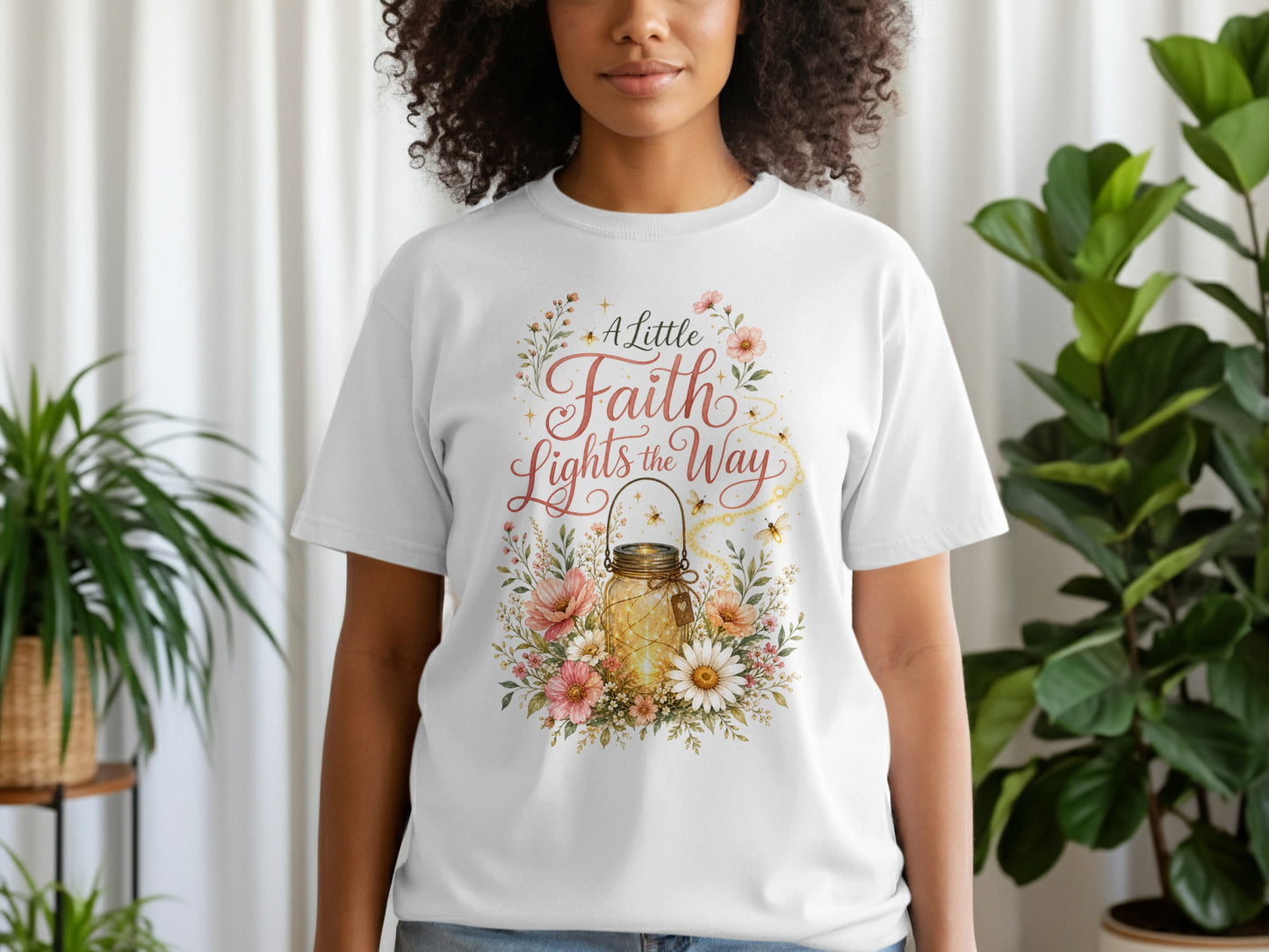 White t-shirt with a floral design featuring a lit mason jar and text "A Little Faith Lights the Way".