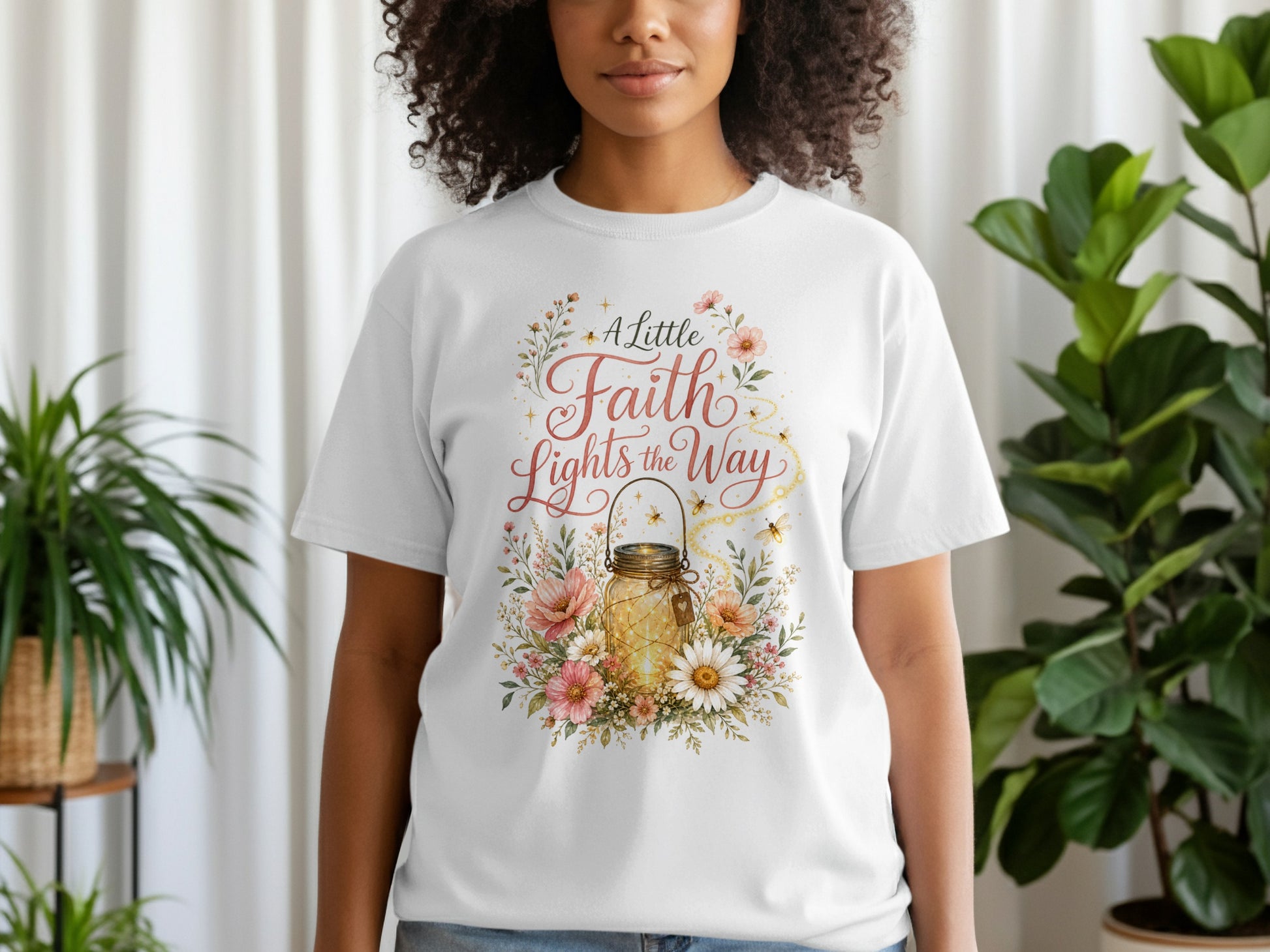 White t-shirt with a floral design featuring a lit mason jar and text "A Little Faith Lights the Way".