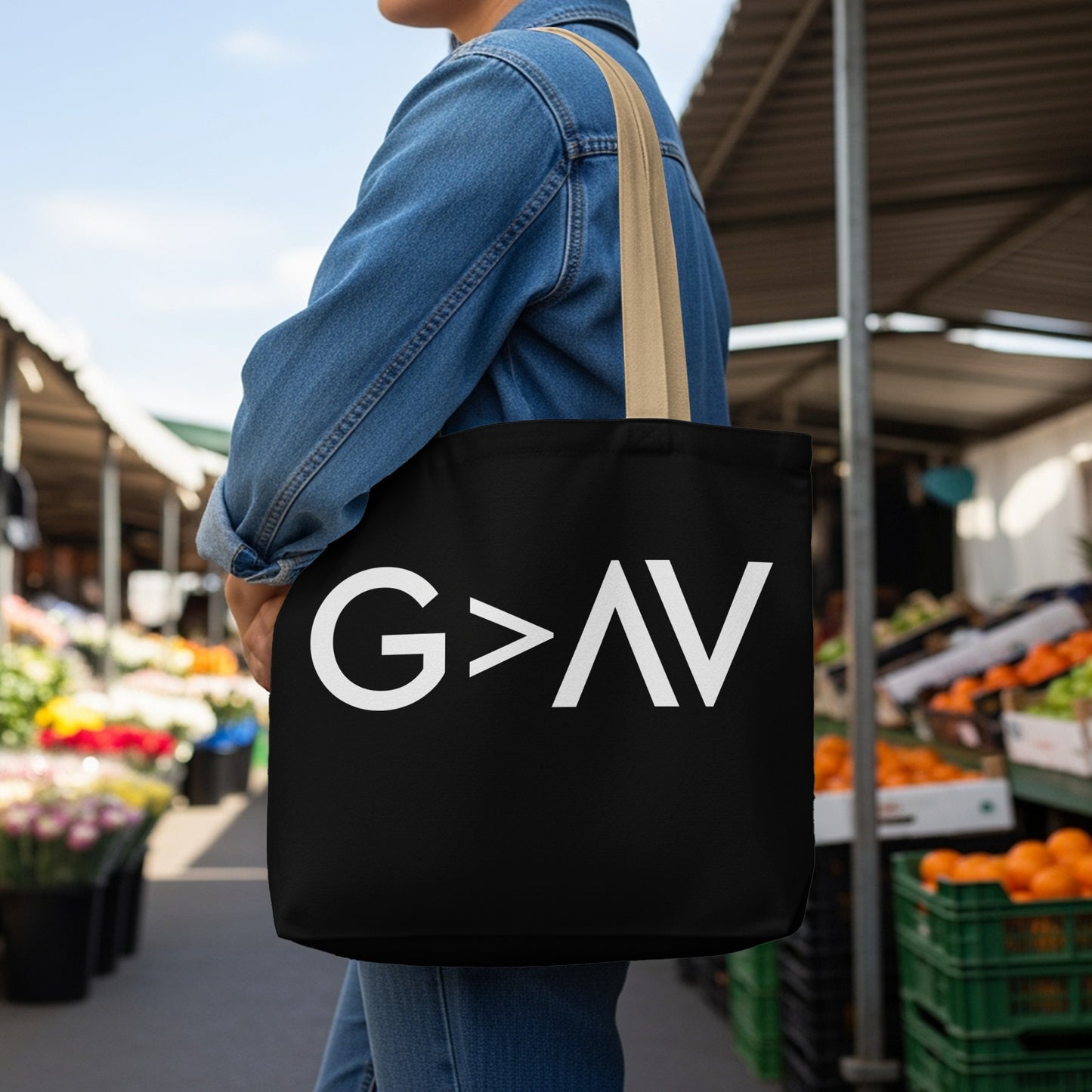 Black tote bag with white text "G>AV" worn by a person outdoors.