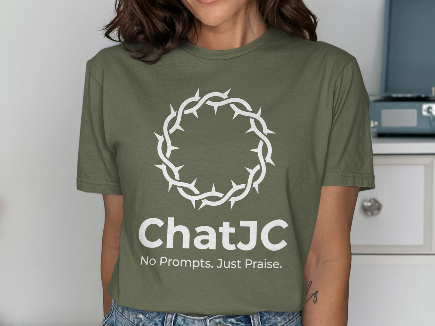 Olive green t-shirt with white crown of thorns and "ChatJC No Prompts. Just Praise." text.