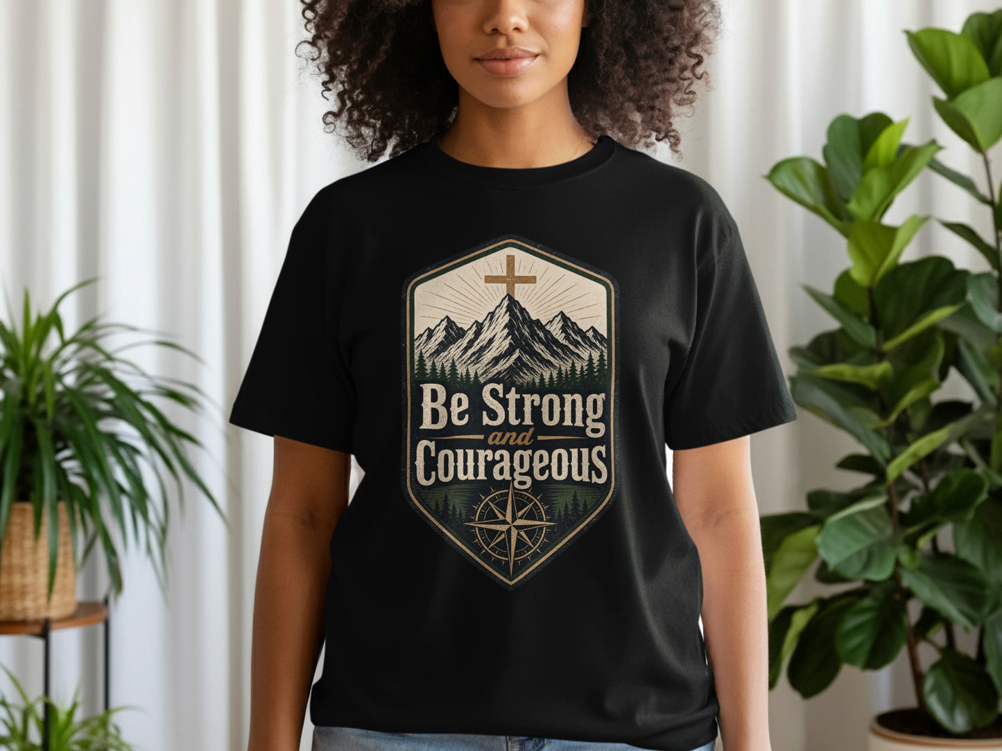 Black t-shirt with a shield graphic featuring mountains, a cross, and the text "Be Strong and Courageous."