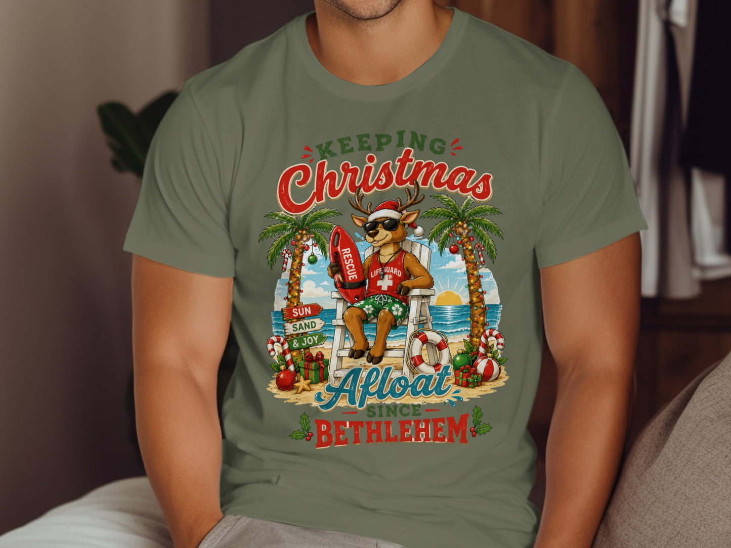 Deer lifeguard in Santa hat sits on beach chair with surfboard, "Keeping Christmas Afloat Since Bethlehem."