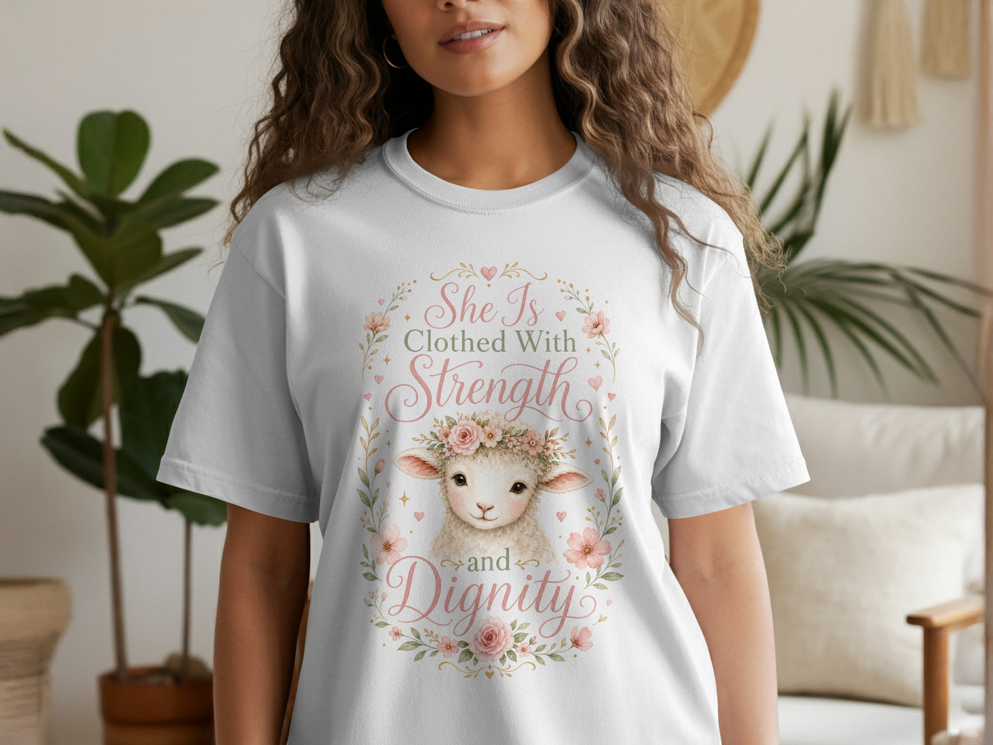 White t-shirt with a watercolor lamb and pink floral wreath with text "She is Clothed With Strength and Dignity".