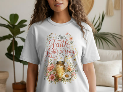 White t-shirt with floral design featuring a lit mason jar and text "A Little Faith Lights the Way".