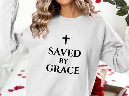 White sweatshirt with black "Saved by Grace" text and a cross graphic.