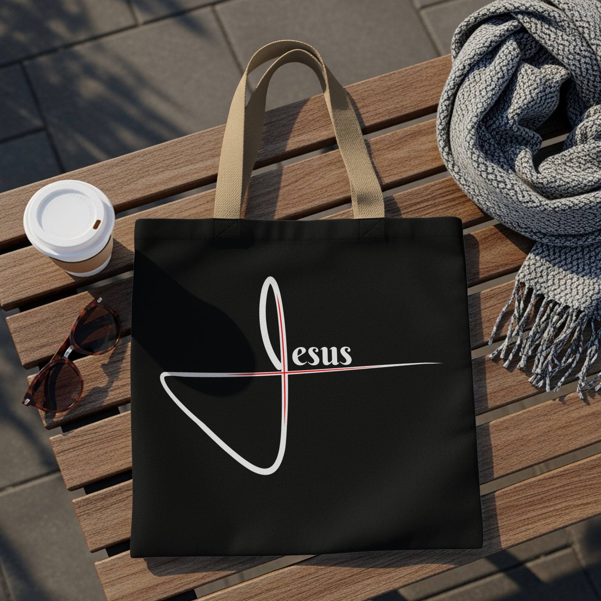 Black tote bag with a white script "Jesus" and red cross detail.