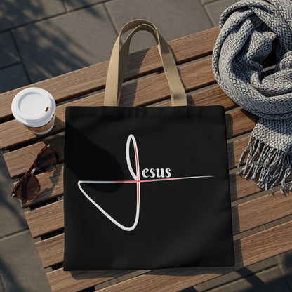 Black tote bag with a white script "Jesus" and red cross detail.