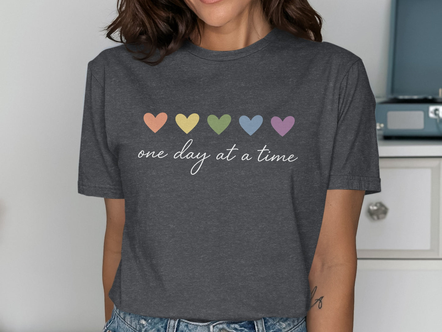 Dark grey t-shirt with pastel heart chain and "one day at a time" text.