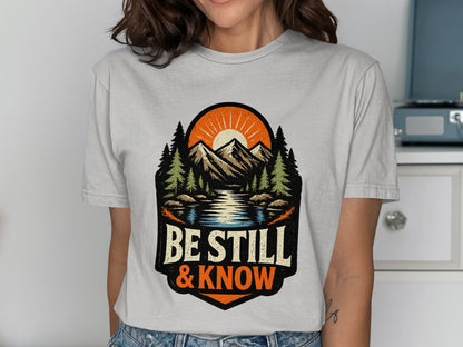 T-shirt graphic with mountains, lake, trees, and "Be Still & Know" text.