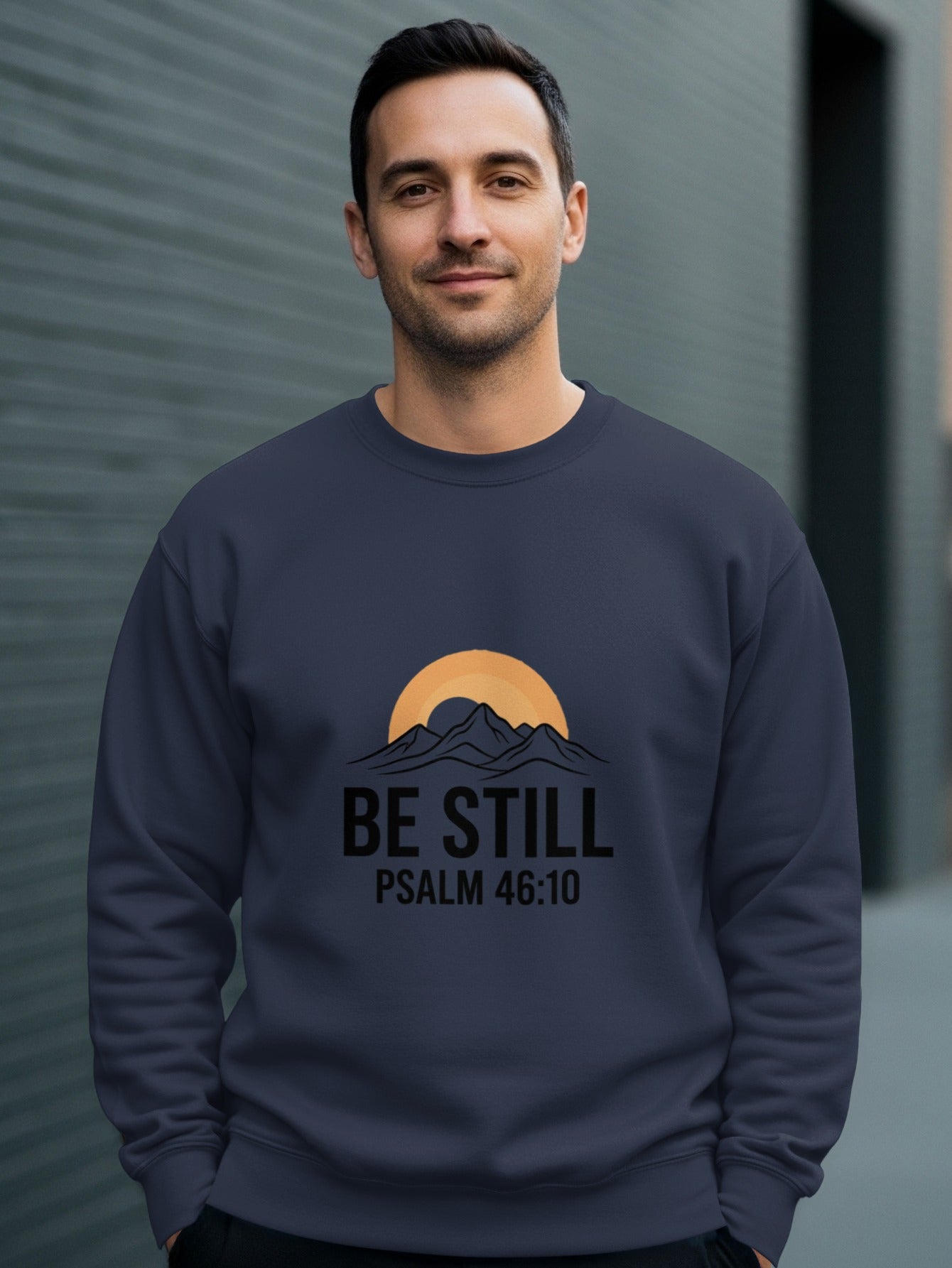 Man wearing a navy sweatshirt with "Be Still Psalm 46:10" text and mountain sunset graphic.