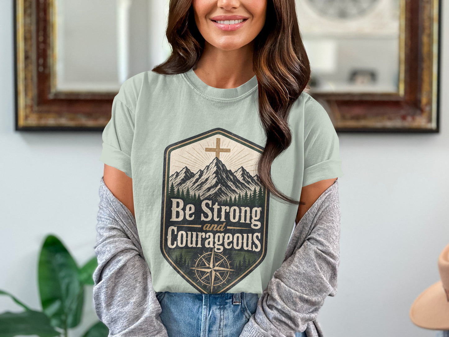 T-shirt graphic with mountains, cross, compass, and text "Be Strong and Courageous."